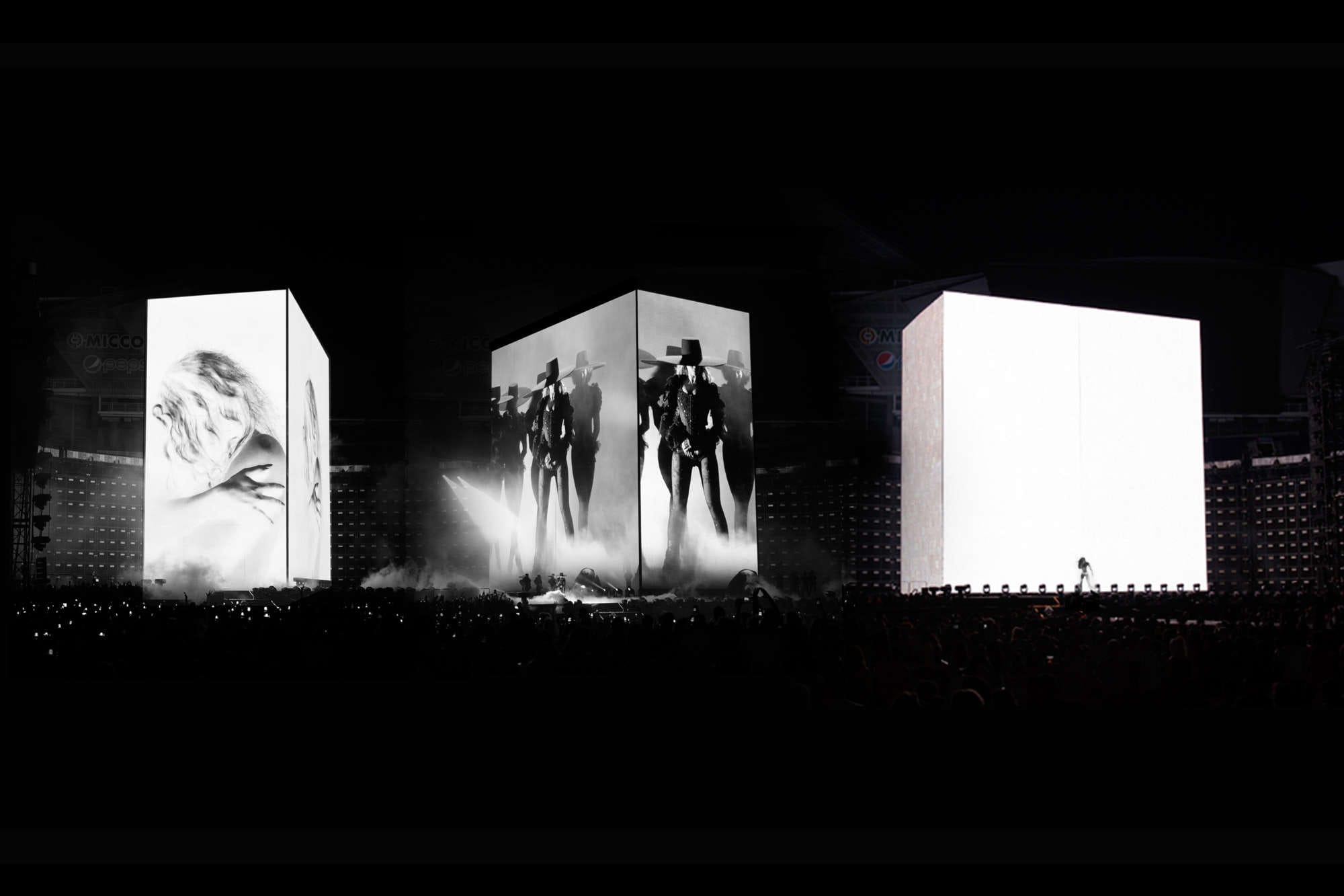 Black and white stage design by Es Devlin featuring monumental illuminated cubes displaying silhouettes of performers during a live concert, blending architecture, light, and performance art