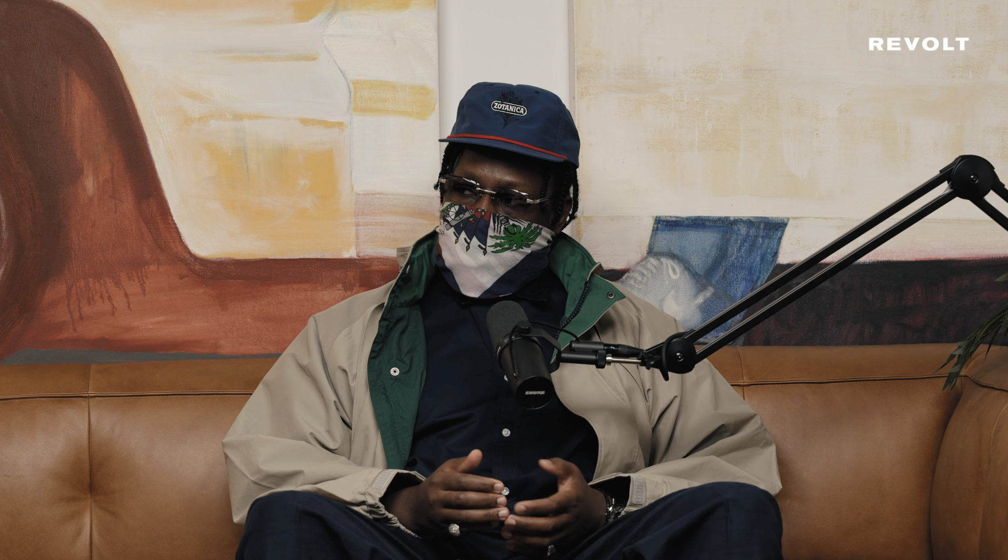 Mach-Hommy seated in the Wrist Check Podcast studio wearing a green jacket and Piaget Altiplano.