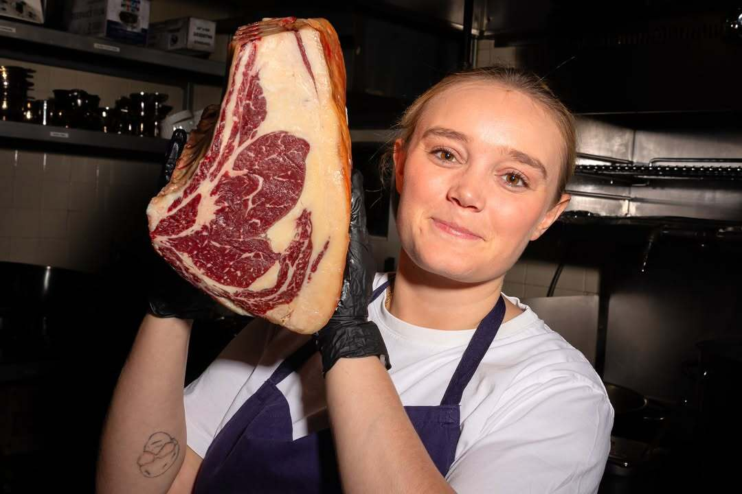 Chef Alexia Duchêne holding a cut of dry-aged beef inside the kitchen at Le Chêne restaurant in NYC.