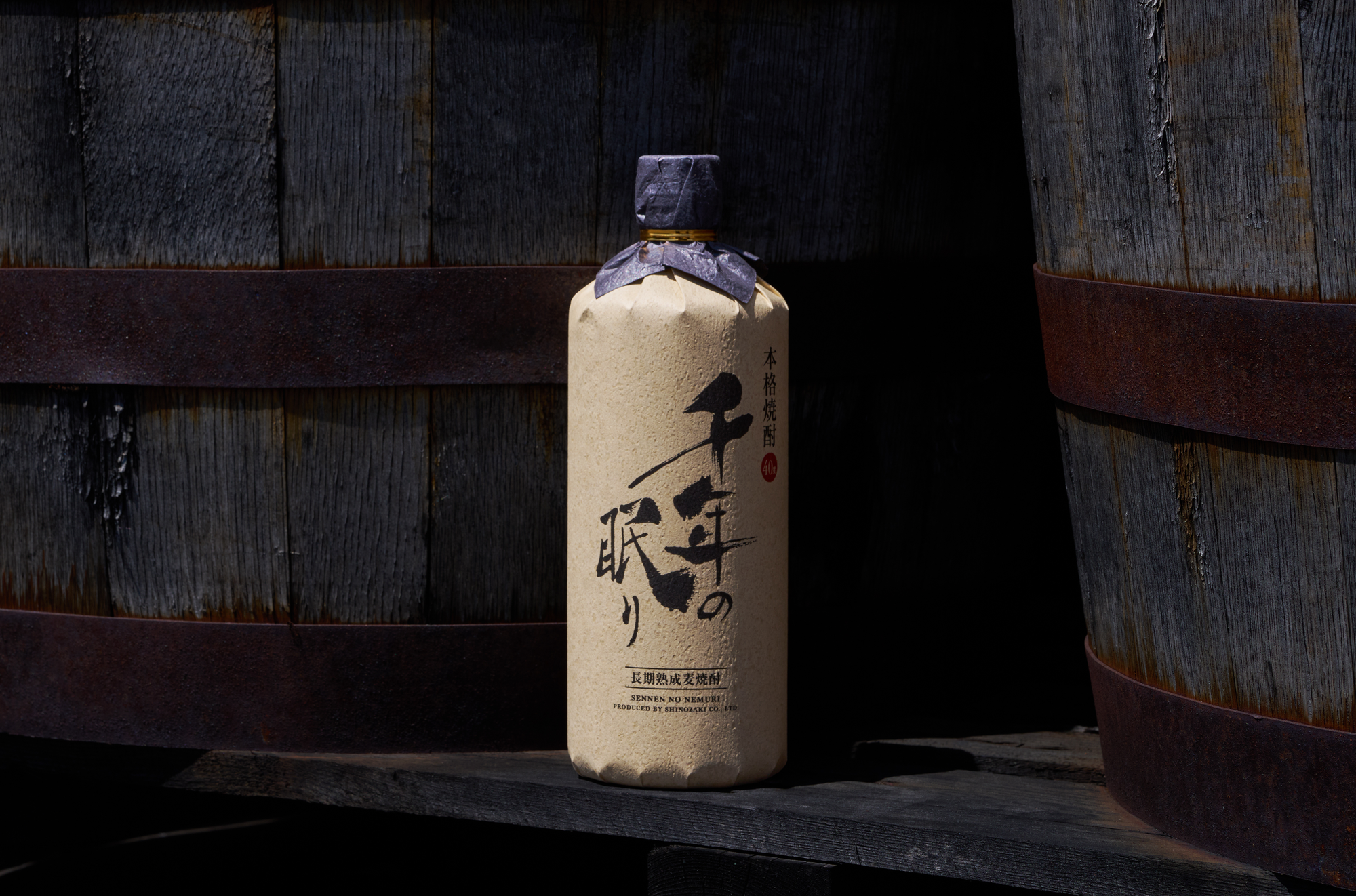 Shindo Experimental 01 whisky bottle positioned between aging barrels, emphasizing the distillery’s focus on process before maturation.