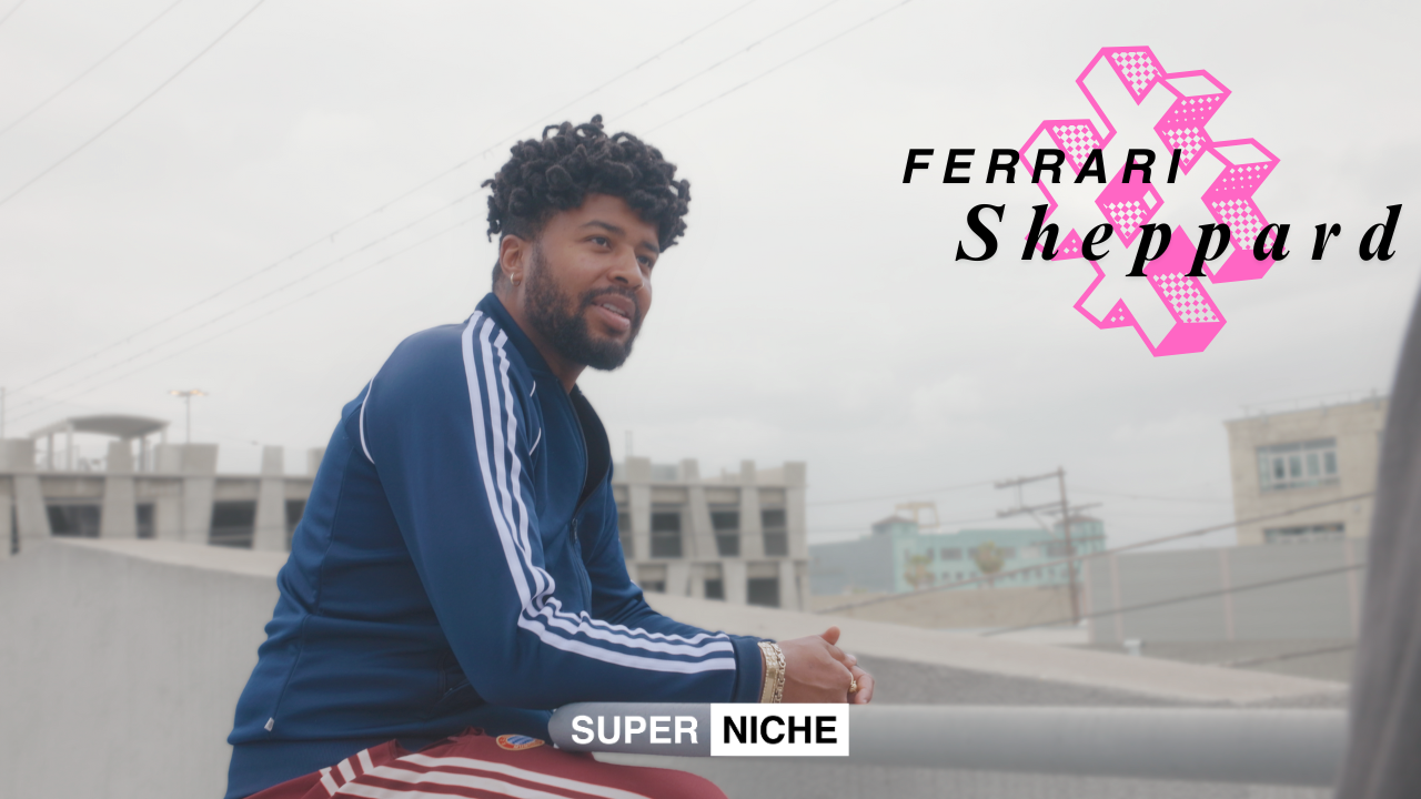 Artist Ferrari Sheppard sitting outdoors in a blue track jacket and red pants, against an urban skyline with his name and the Super Niche logo overlayed on the image.