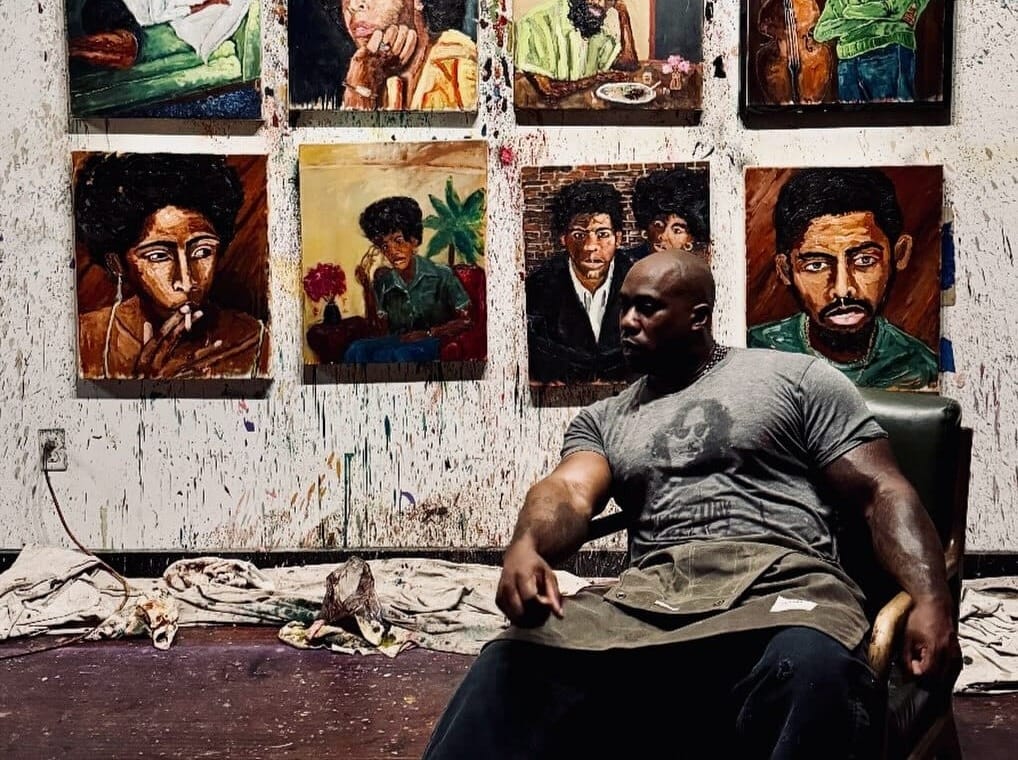 Ronnie Robinson sitting in an armchair in front of his paintings.