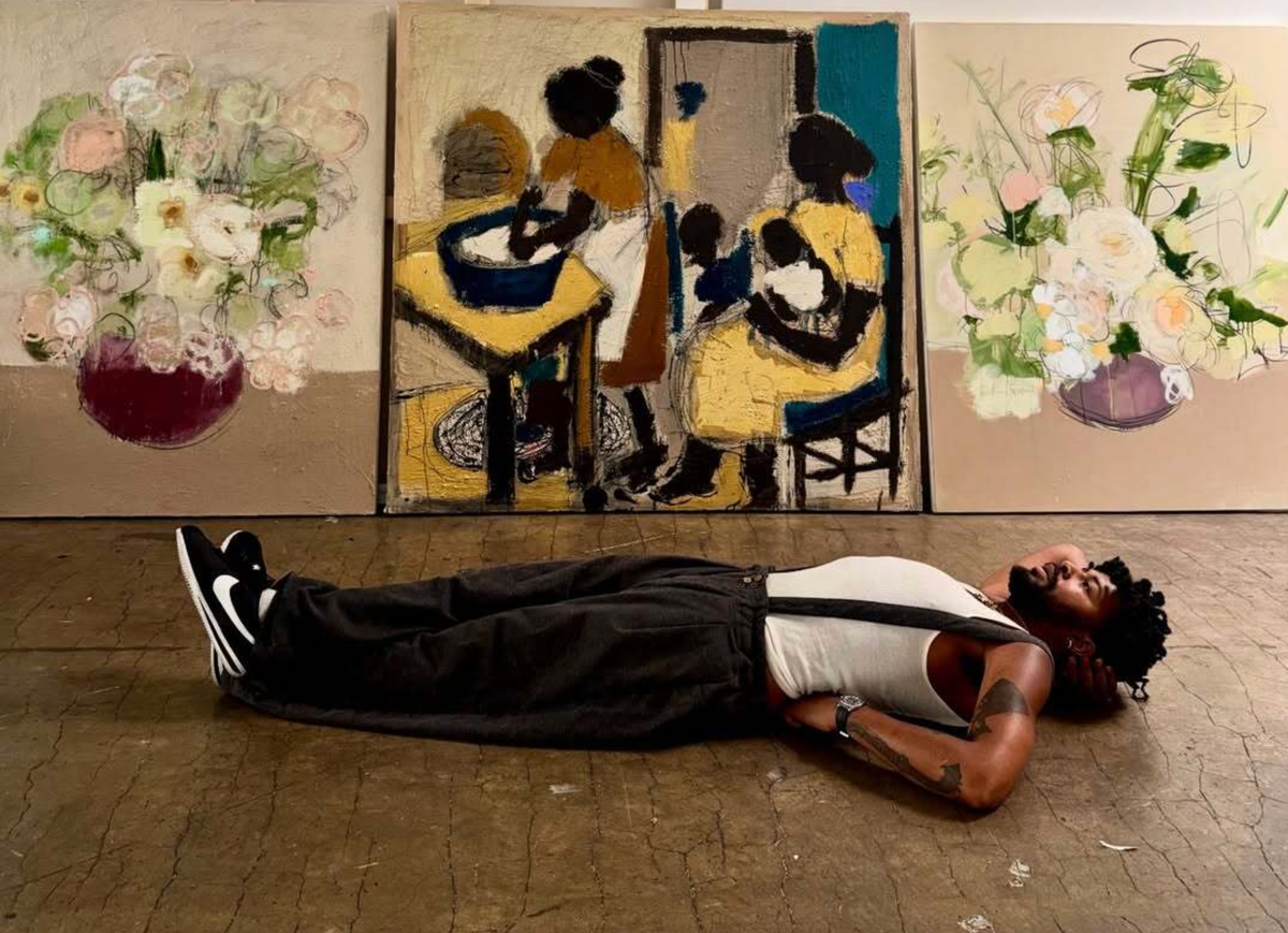 Ferrari Sheppard laying down on the floor in front of his paintings, one arm under his head, second one under his back.